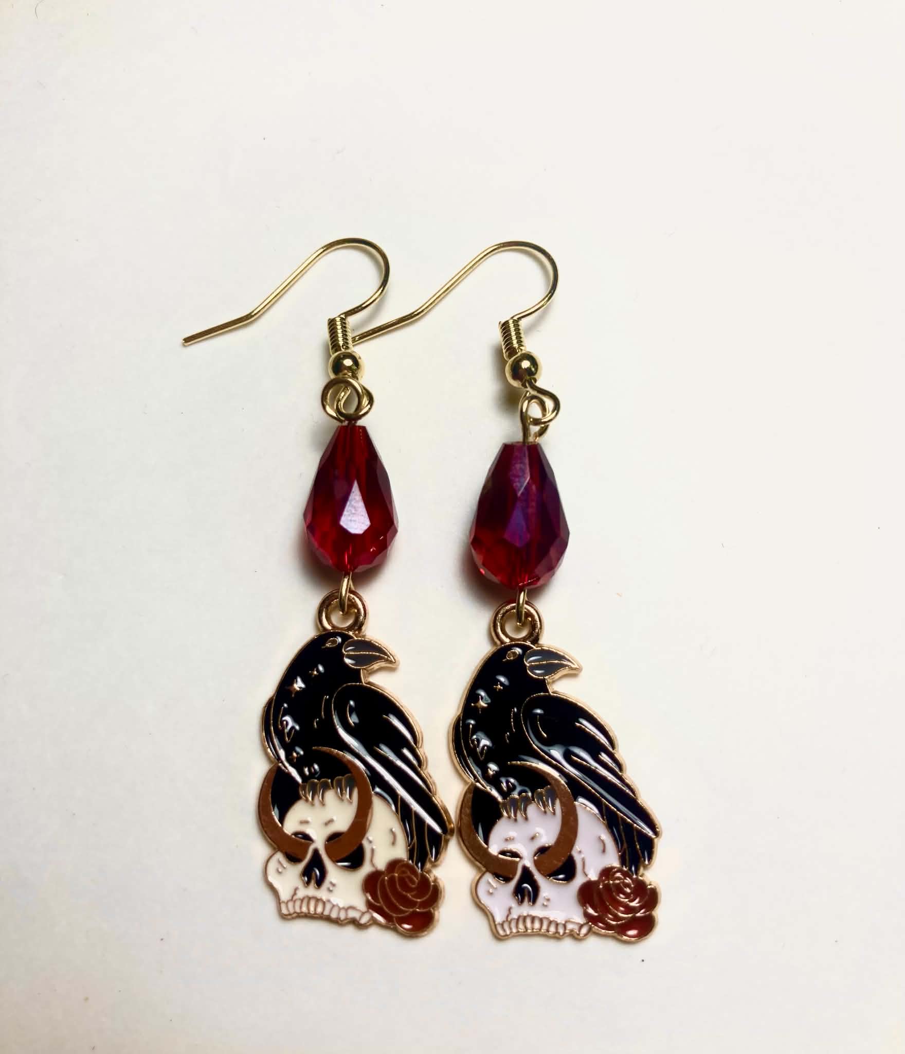 Black enamel raven perched on white skull with red roses drop earrings with dark red Czech glass teardrop beads and 14k gold plated hooks