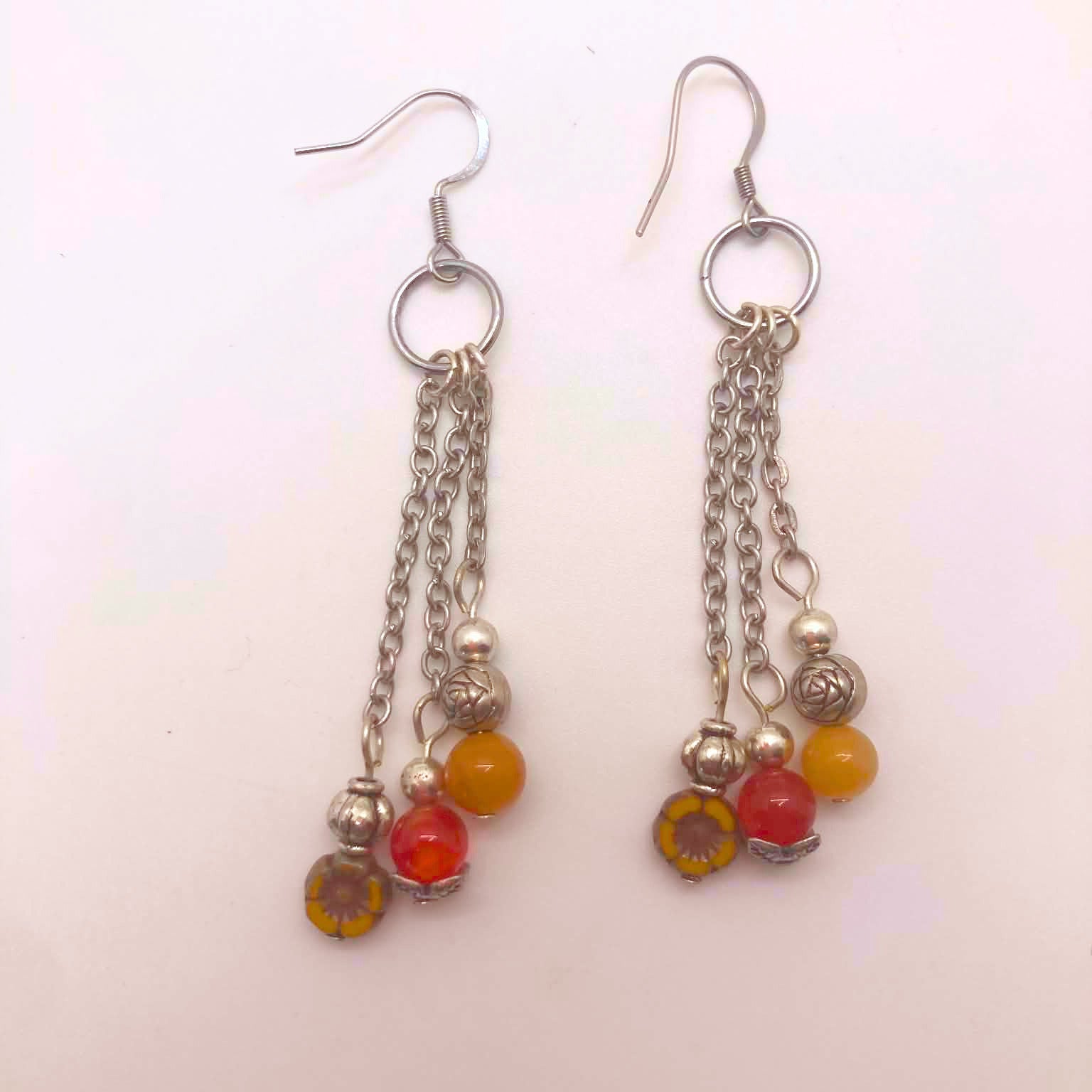 Triple chain dangle earrings with yellow agate, red carnelian, and Czech glass flower beads on white background