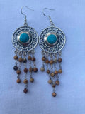Pair of silver earrings with turquoise stones and picture jasper beads on a light blue background