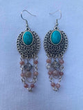Pair of earrings with turquoise stones and pink beads on a light blue background
