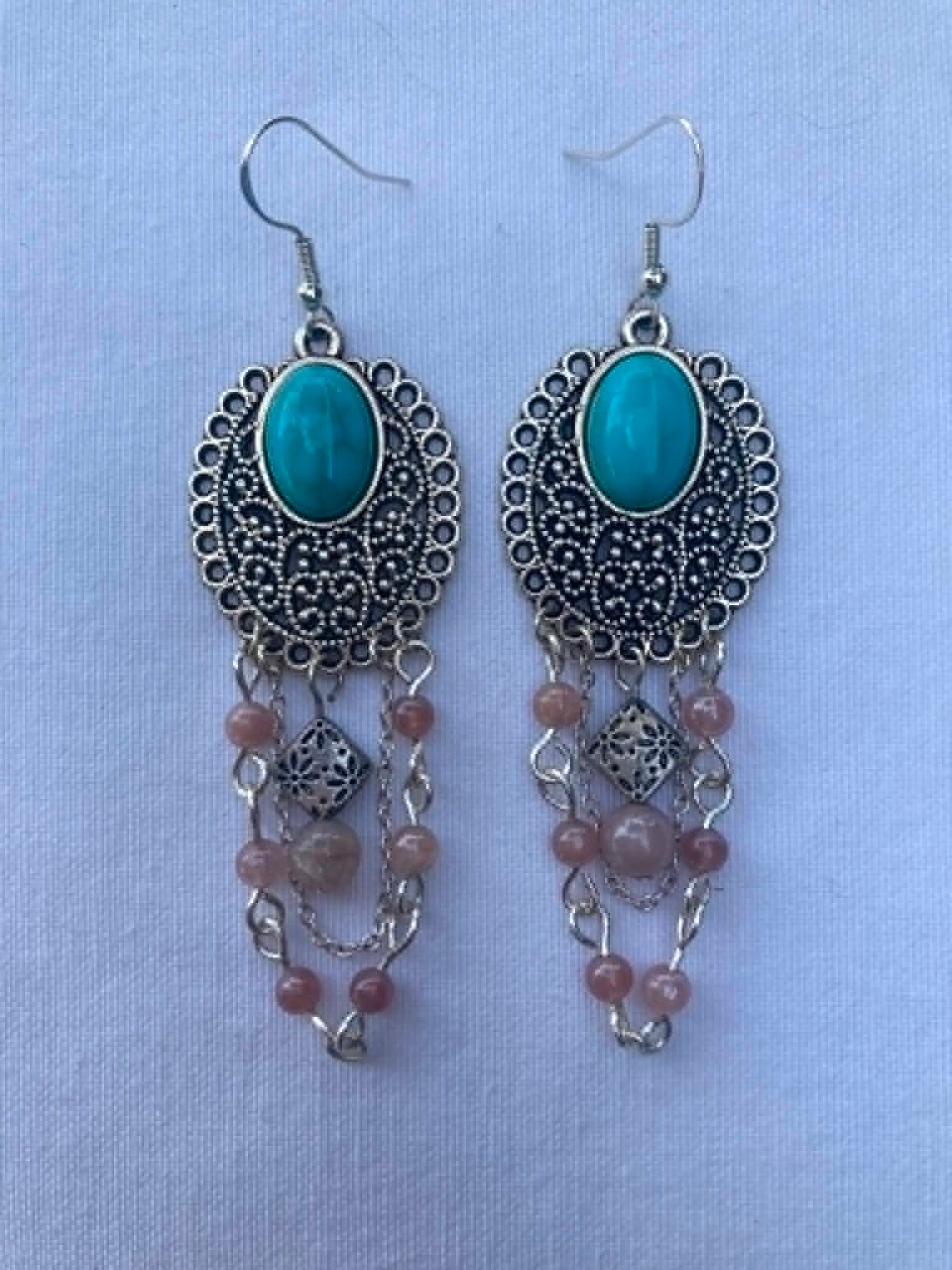 Pair of earrings with turquoise stones and pink beads on a light blue background