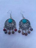 Pair of ornate earrings with turquoise stones and bead accents on a light blue background