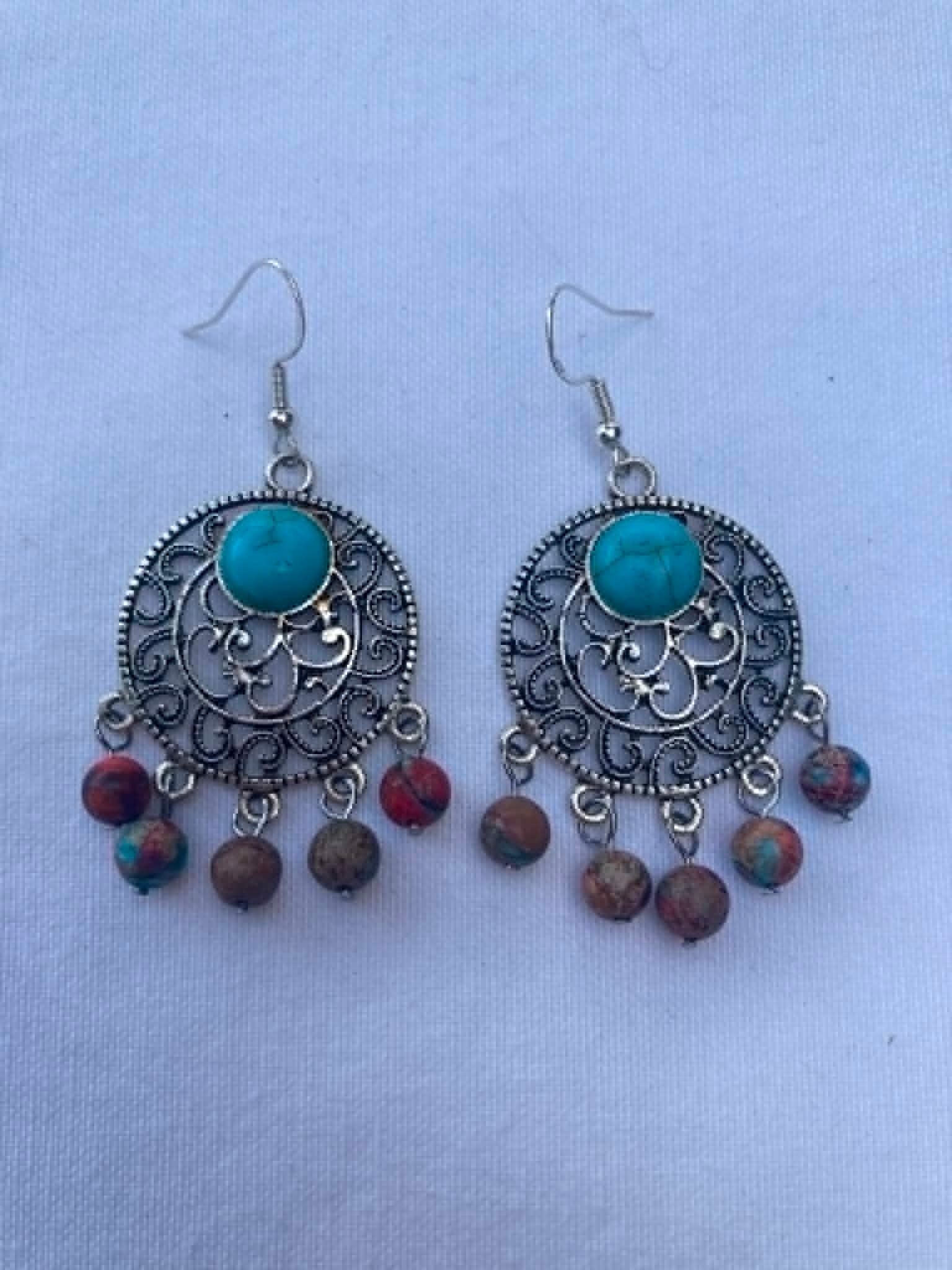 Pair of ornate earrings with turquoise stones and bead accents on a light blue background